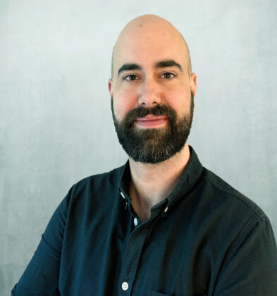 A picture of Frank Sparrer, senior marketing manager for Beam. He is a white, bald male with a dark beard and dark eyes. He is smiling, wearing a dark green shirt against a light grey background