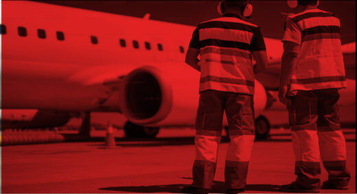 Two ground crew stand on the tarmac in front of a parked jetliner